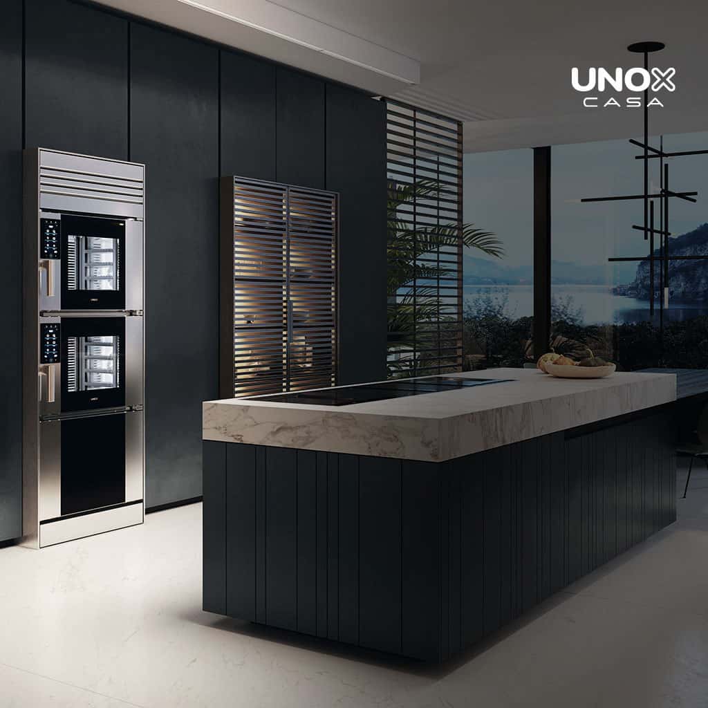 Luxury home kitchen with a large marble countertop and a view of the ocean from the window, with a built-in combi oven, stacked on top of another. 