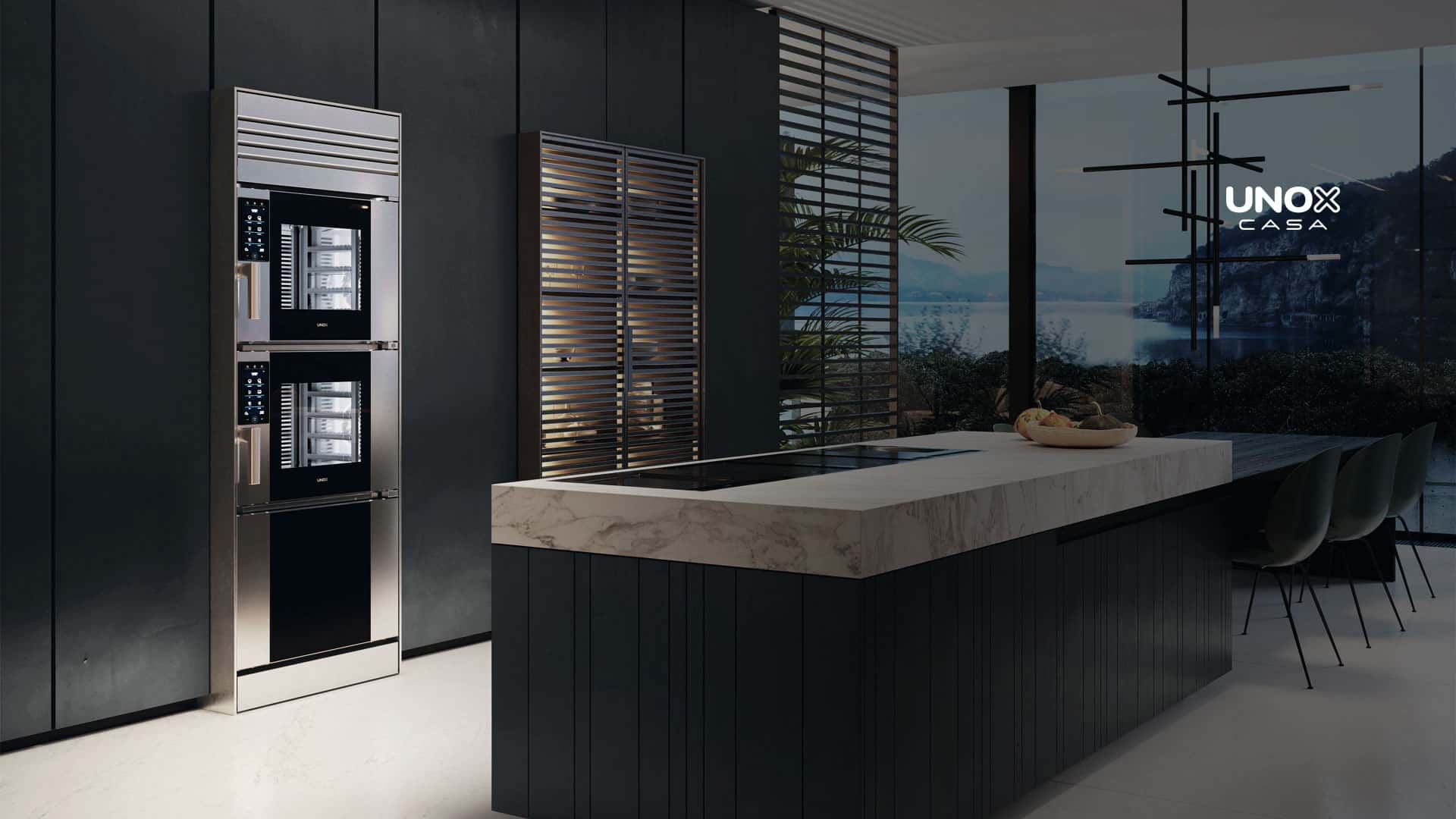 Luxury home kitchen with a large marble countertop and a view of the ocean from the window, with a built-in combi oven, stacked on top of another. 