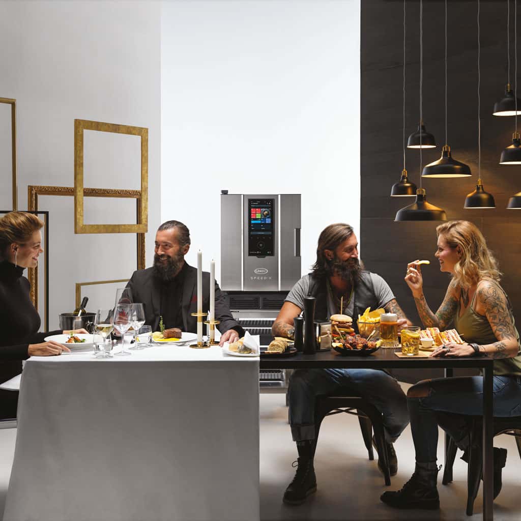 A large dining table, with two couples. One couple are eating fine dining and the other are eating burgers. An Unox speed oven is in the centre.