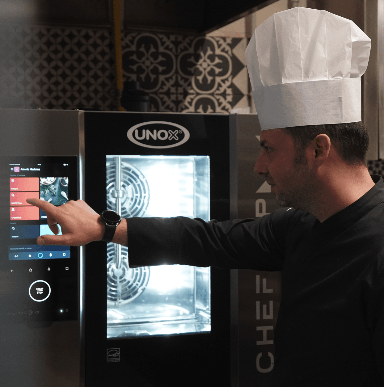 Chef using the touchscreen control panel of a Unox smart commercial oven in a restaurant kitchen