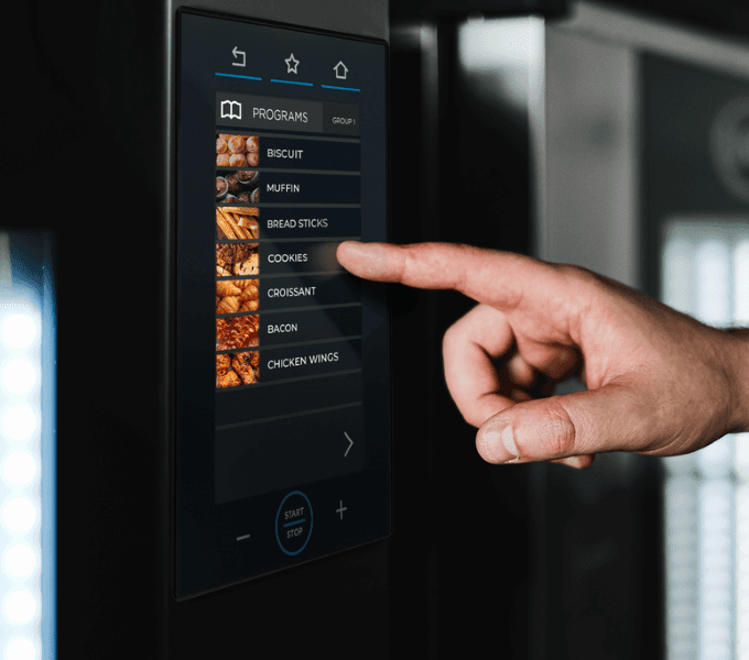 Hand selecting a cooking program on the digital control panel of a Unox commercial combi oven.