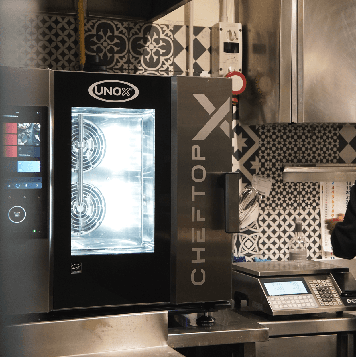 Unox smart combi oven with the touchscreen display on, placed on a commercial kitchen counter next to a scale