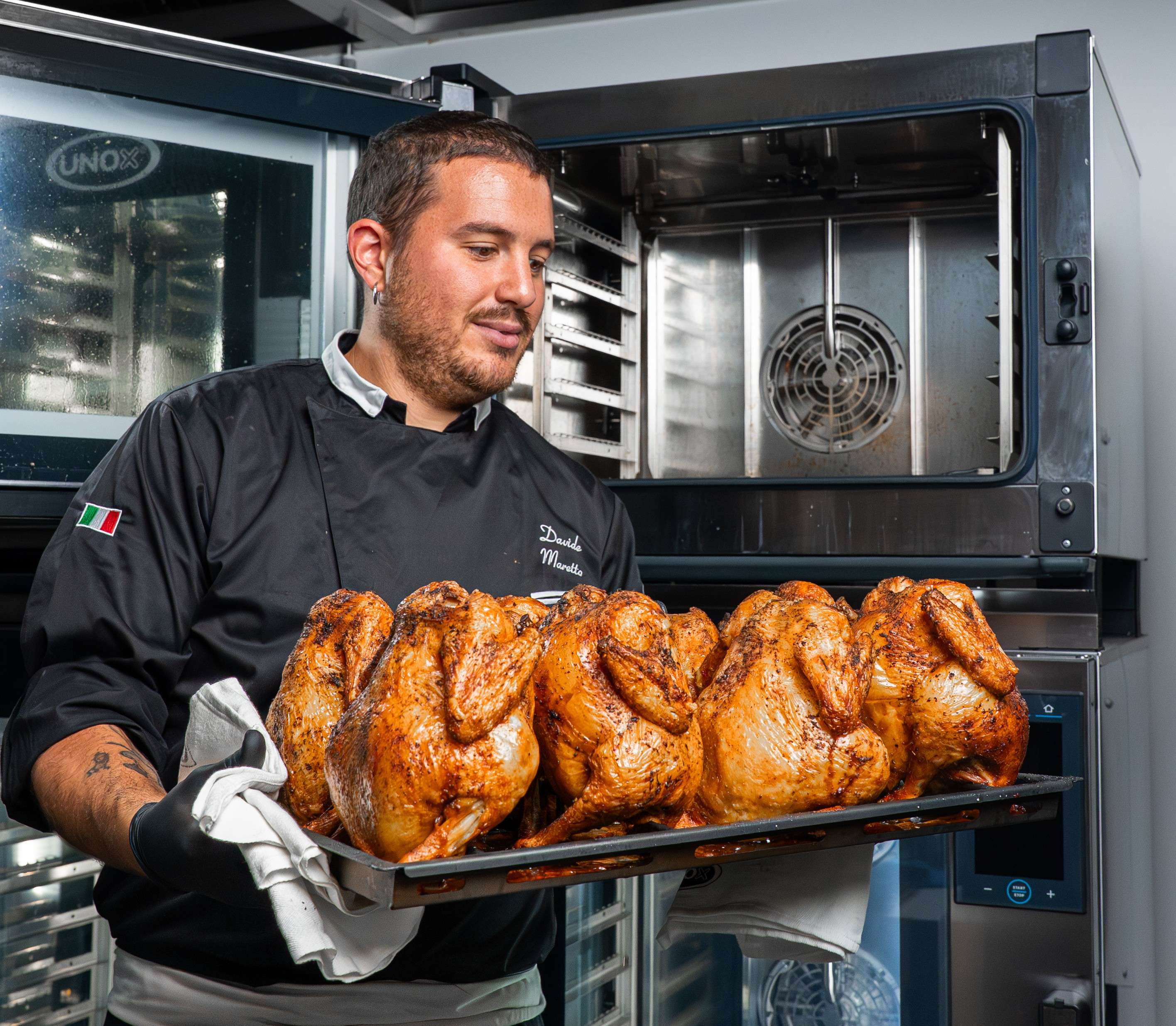 male chef looking at a tray of roasted chickens just removed from the Unox commercial combi oven behind him