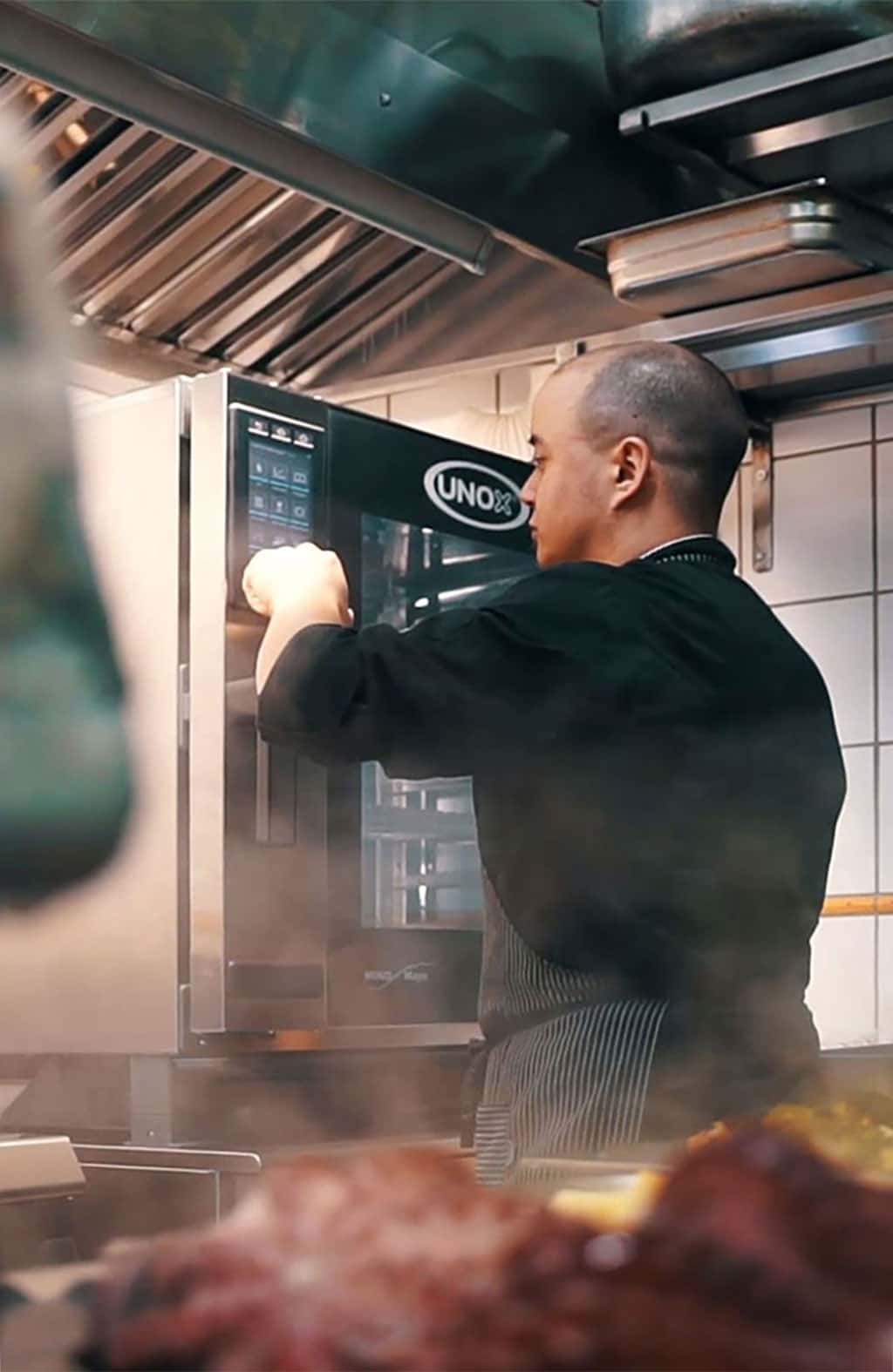 Male chef in kitchen pressing buttons on display of an Unox combi oven.