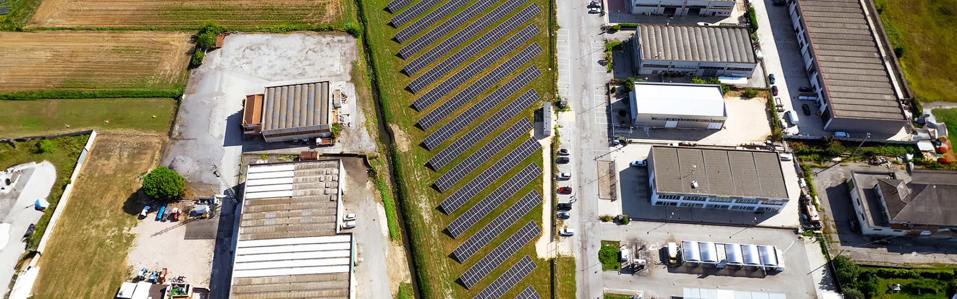 Overhead photo of field of solar panels amongst a block of buildings and surrounded by green fields.