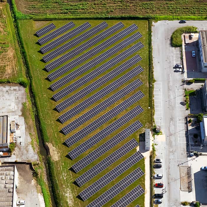 Overhead photo of field of solar panels amongst a block of buildings and surrounded by green fields.