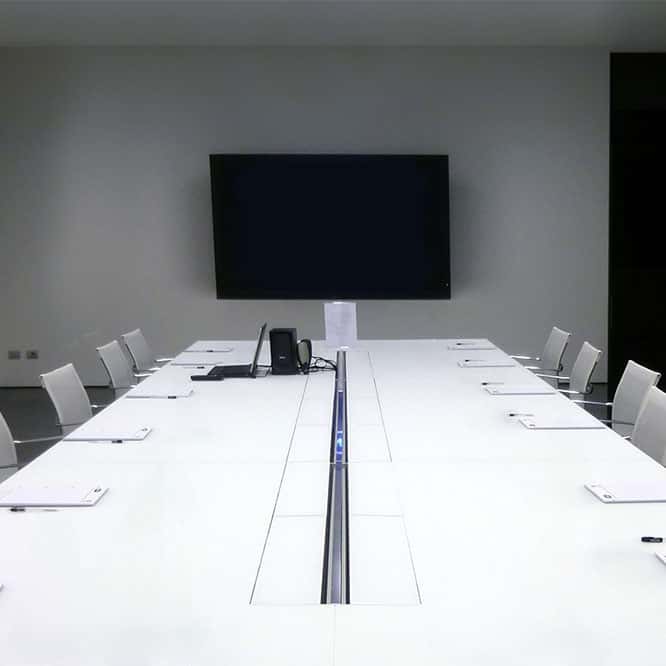 An office boardroom with a long white table in the middle, lined with white office chairs, white pads of paper and pens placed at each seat.