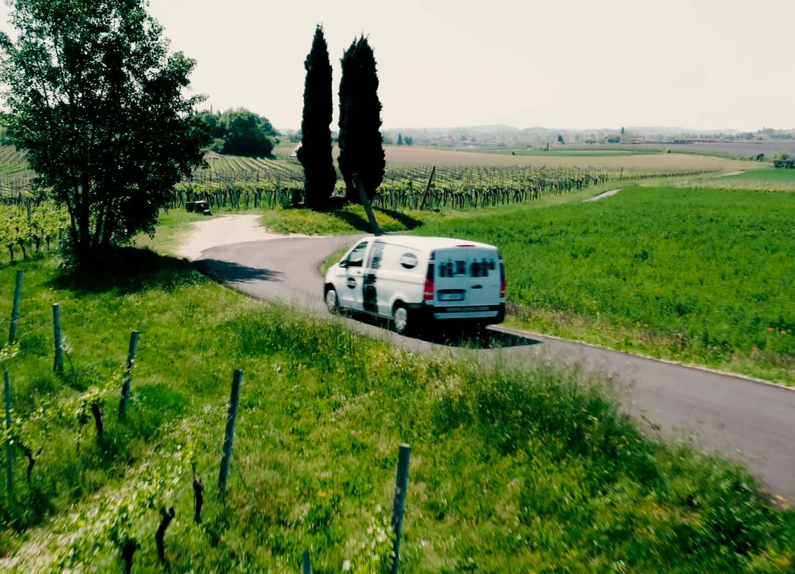White van with Unox logo and images printed on drives down a road surrounded by green fields and trees.