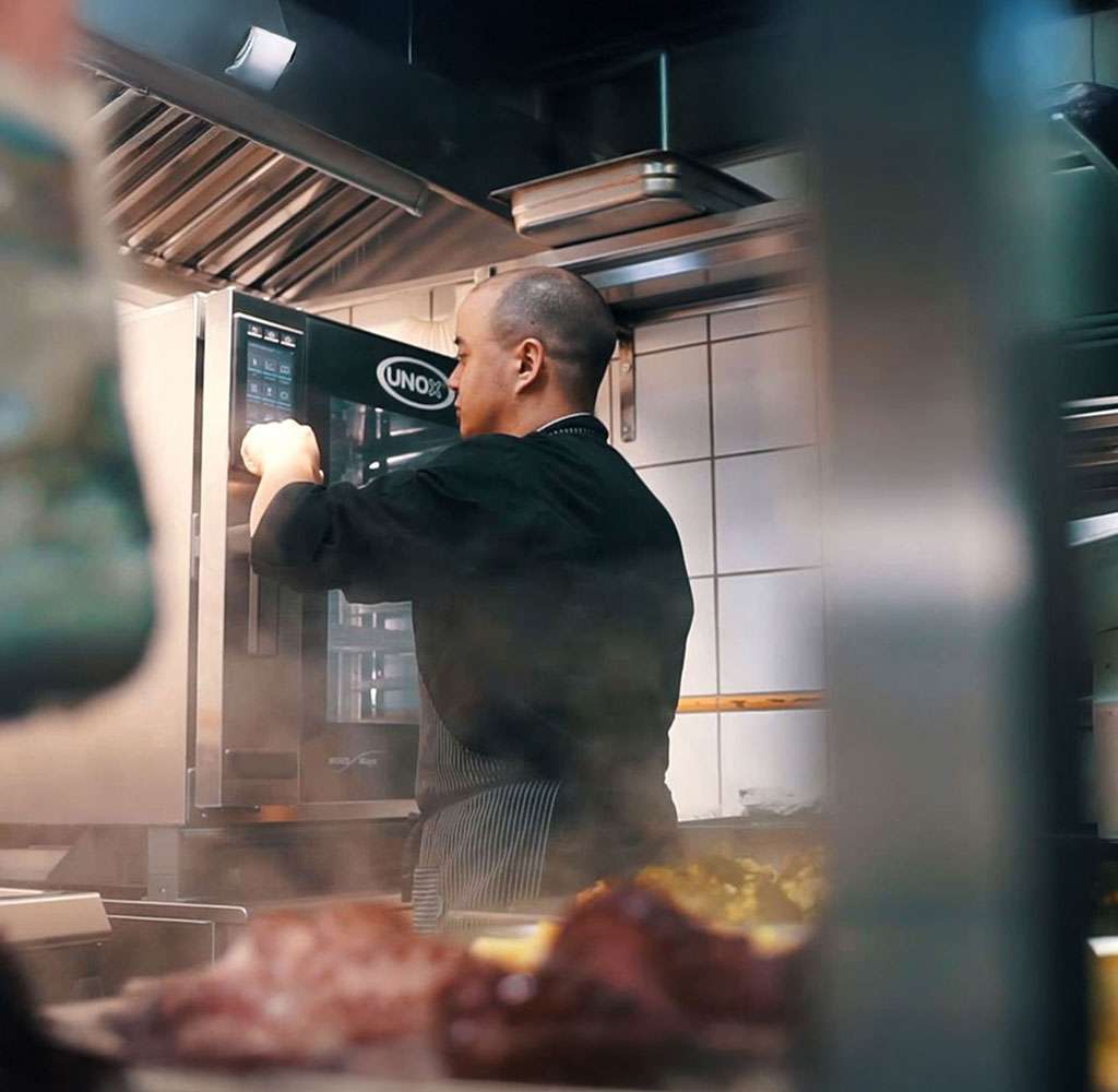 Male operator using the touch panel of a Unox commercial combi oven in the back area of a deli