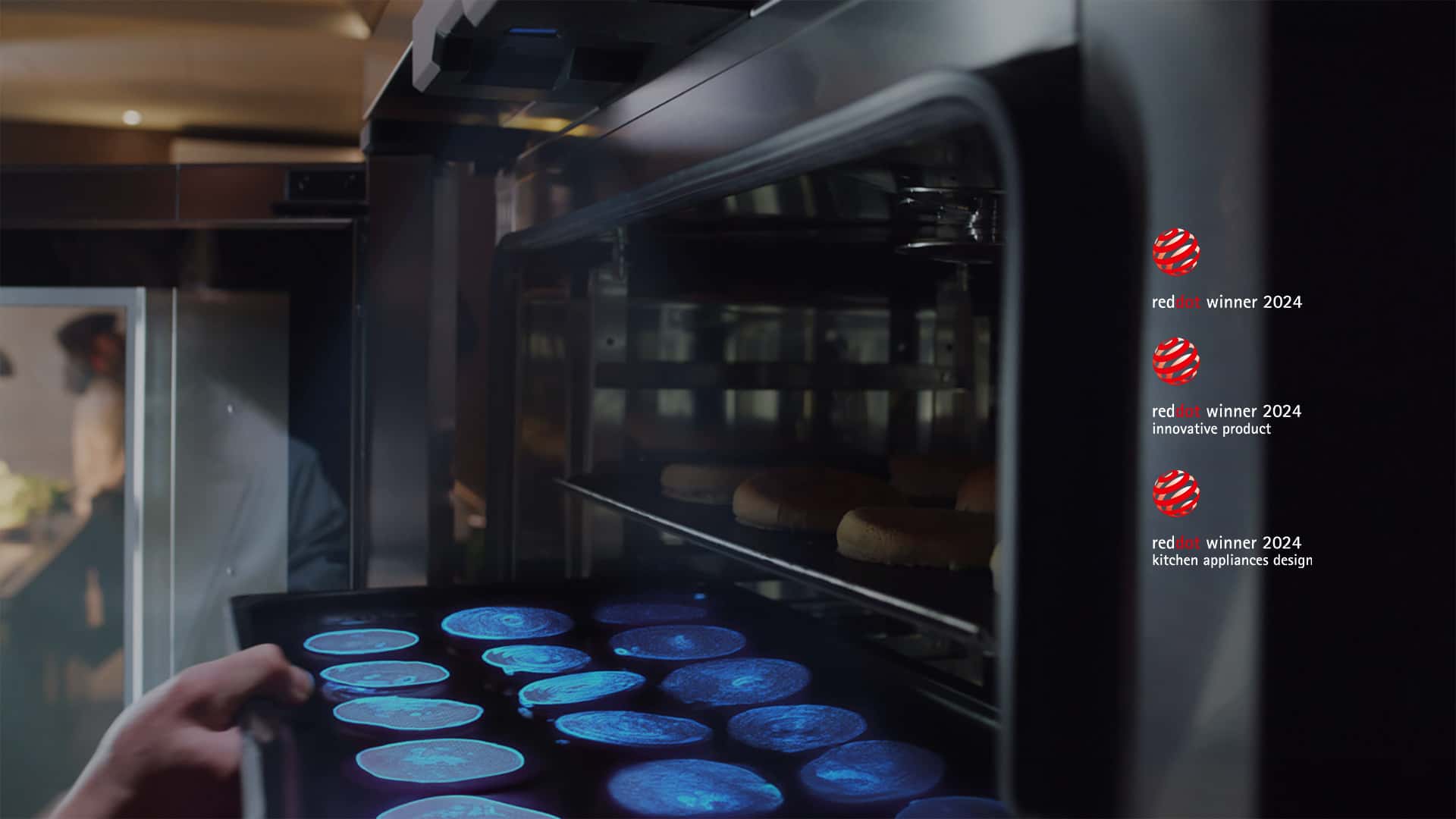 A hand puts a tray of food into an oven. A sensor at the top shines a blue light on the food to scan and identify what the food is.