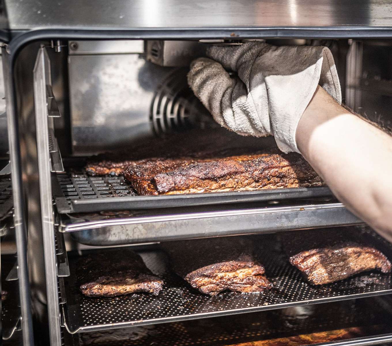 An open cooking chamber of a Unox commercial combi oven with pork ribs inside and a smoking accessory installed
