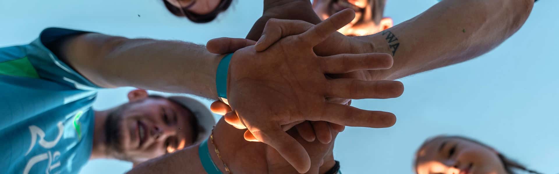 A group of people looking down at the camera, putting their hands in on top of each others', symbolising team work.