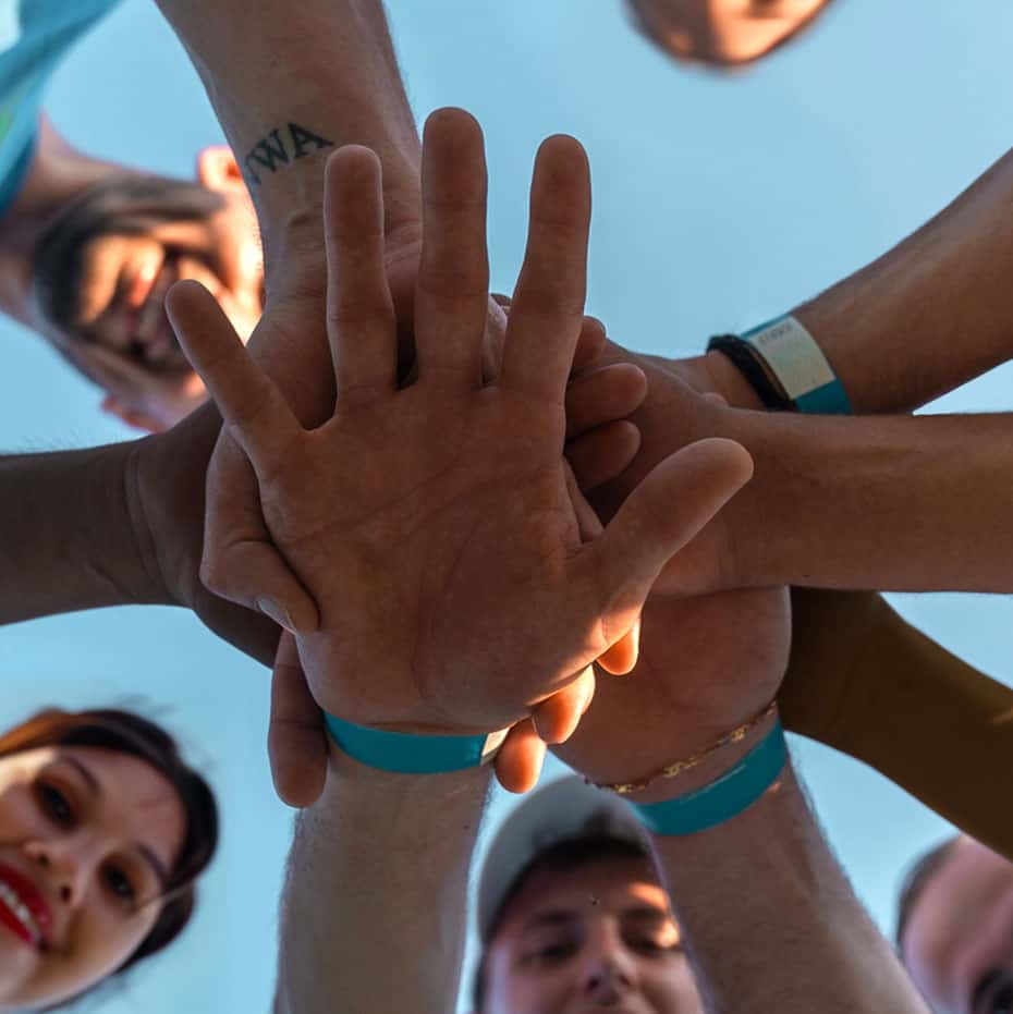 A group of people looking down at the camera, putting their hands in on top of each others', symbolising team work.