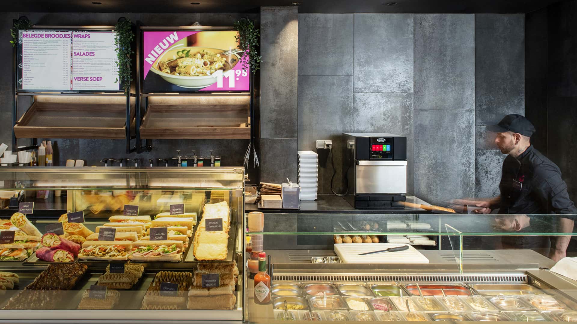 QSR male operator looking at an Unox speed oven behind a counter with wraps, sandwiches, and salads.