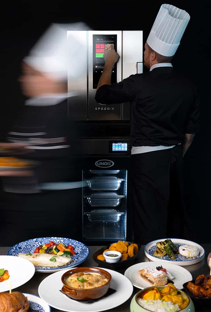 Male chef touching display panel on speed oven, stacked on top of an Unox Evereo, a chef walking fast holding plates of food.